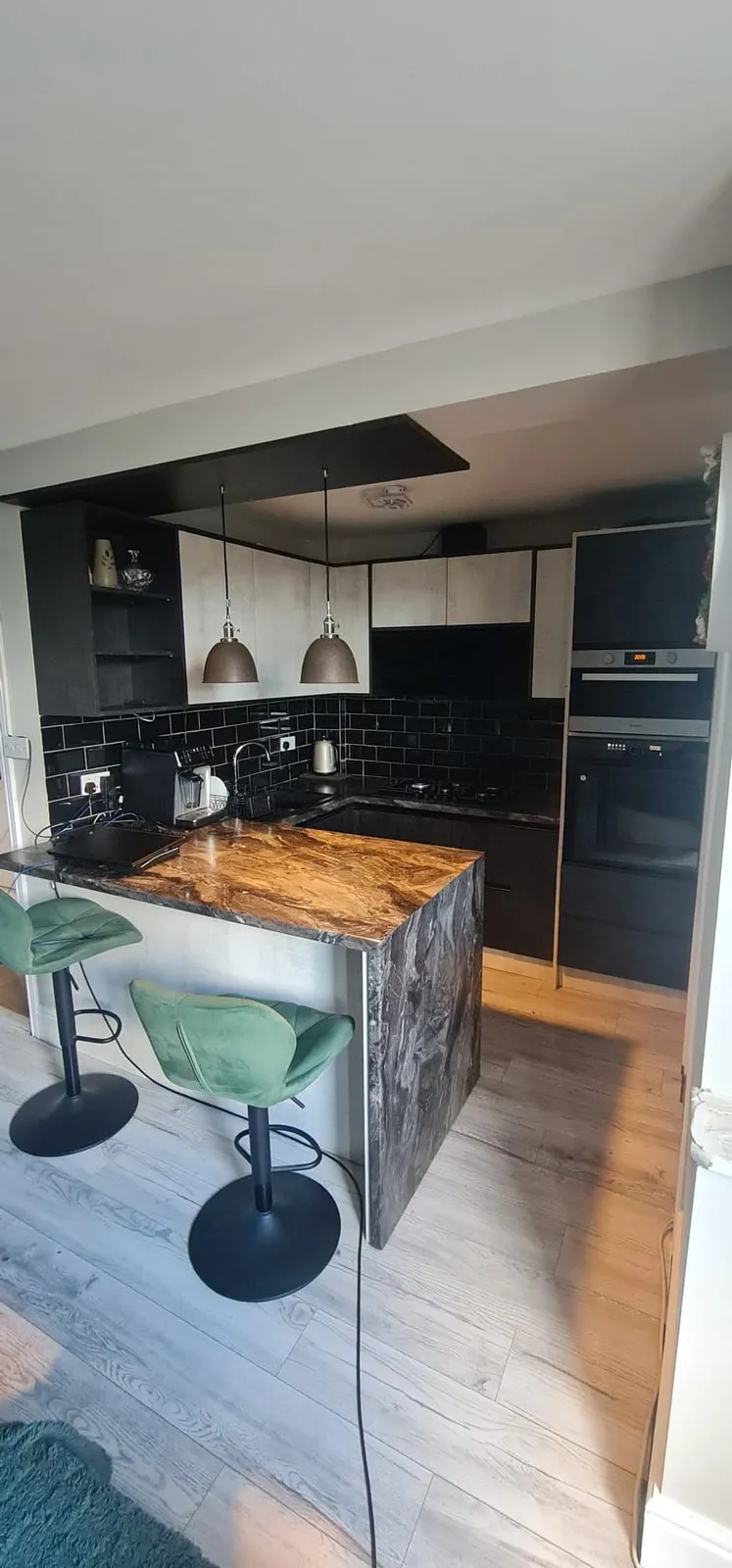 Black kitchen with a stone-effect island, pendant lights and integrated ovens