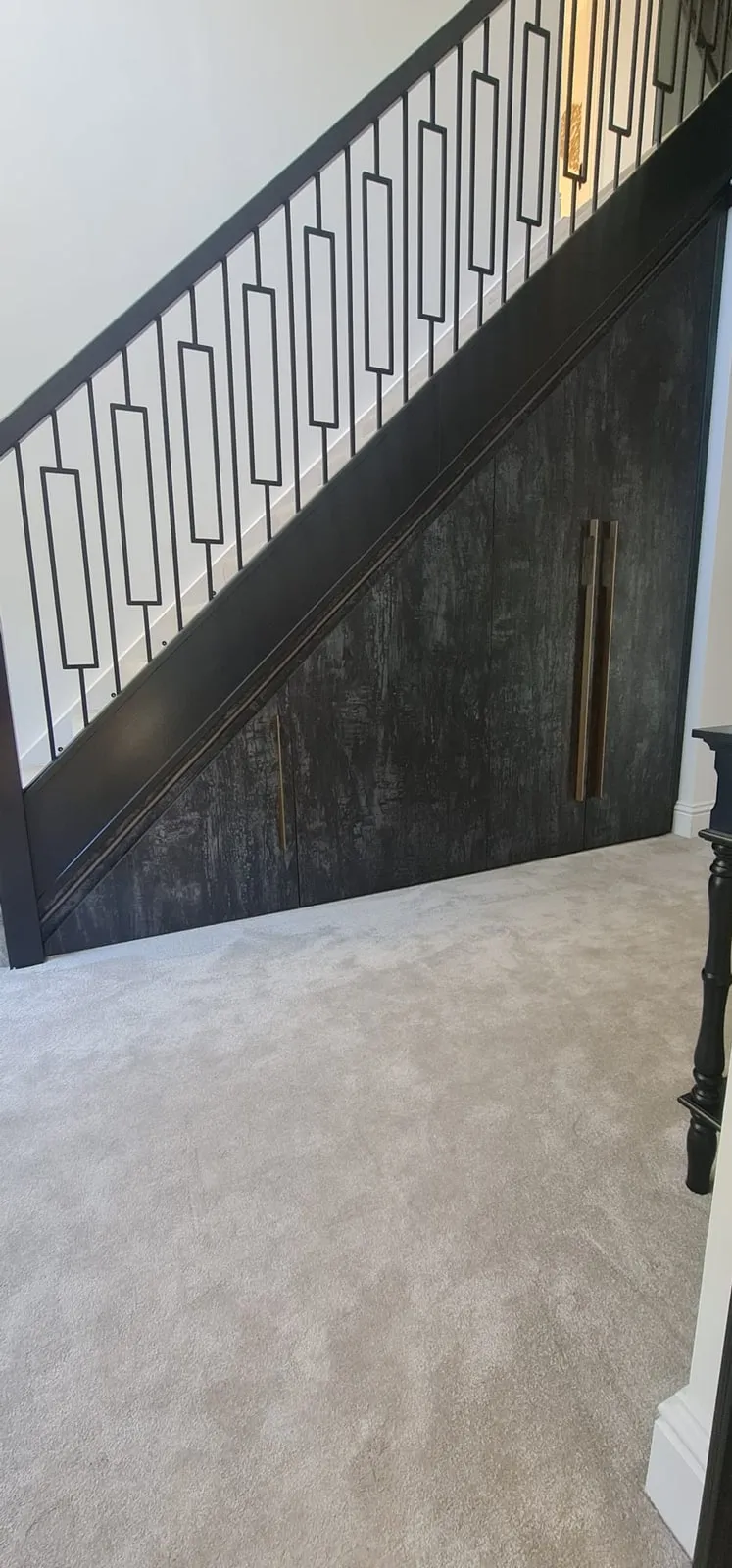Dark under-stairs cupboards with long brass handles, fitted to the slope of the staircase